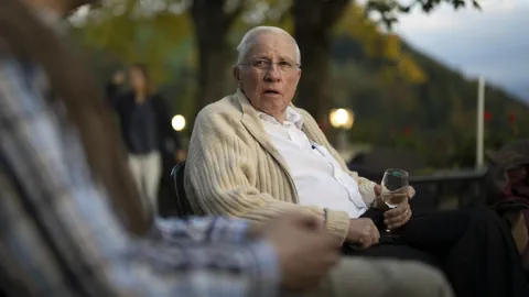 Christoph Blocher im Seitenporträt mit einem Glas Wein in der Hand.