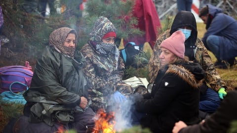 Frauen sitzen dick eingepackt um ein Feuer.