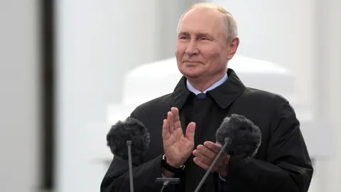 Man in dark jacket clapping behind microphones.