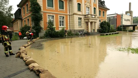 Feuerwehrleute beobachten Hochwasser auf einer Strasse, das Hochwasser wird durch Sandsäcke begrenzt