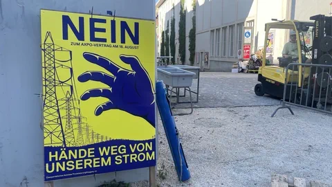 Protestplakat gegen Stromabkommen mit grosser Hand neben Baustellenszene.