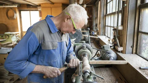 Mann mit weissem Haar arbeitet an Drechselmaschine