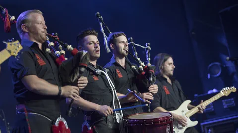 Die Red Hot Chilli Pipers spielen auf einer Bühne Dudelsack, E-Gitarre und die Trommel.