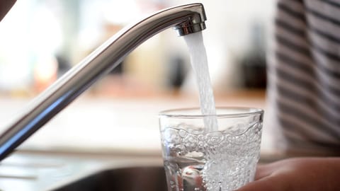 Auf dem Bild ist eine Frau zu sehen, die ein Glas Wasser füllt.