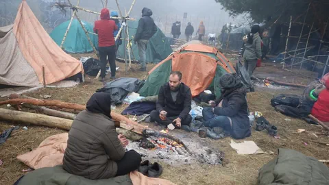 Flüchtlinge sitzen vor Zelten an einem Feuer.