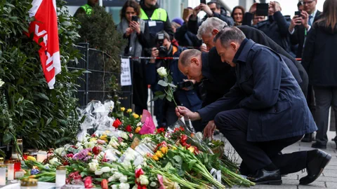 Männer legen Blumen an einer Gedenkstätte nieder.