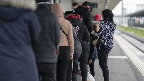 Flüchtlinge stehen an einem Bahnhof.