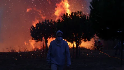 Ein Mann steht vor lodernden Flammen in der Abenddämmerung.