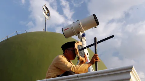 Mann beobachtet vor einer Moschee den Himmerl mit einem Teleskop.