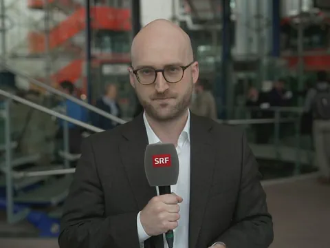 Ein Reporter steht mit einem Mikrofon bereit.