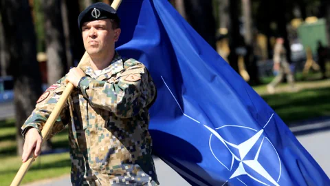 Soldat in uniform trägt NATO-Flagge.