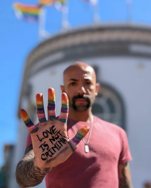 Ein Mann hält seine bemalte Hand in die Kamera. Darauf steht «Love is not a criminal!»