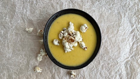 Eine Maissuppe mit Popcorn in einem schwarzen Teller, von oben fotografiert.