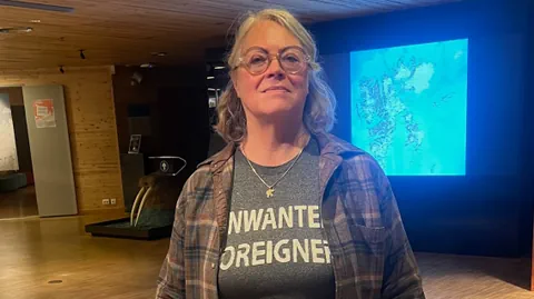 Elisabeth  Bourne blickt in die Kamera. Sie trägt ein graues T-Shirt mit der Aufschrift «Unwanted Foreigners».