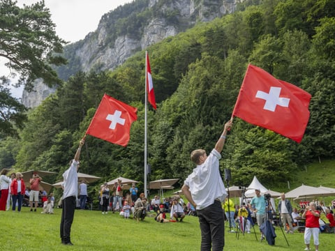 Menschen schwenken schweizerische Fahnen bei einer Feier im Freien.