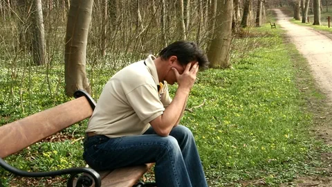 Mann sitzt auf Bank und stützt Kopf in die Hände.