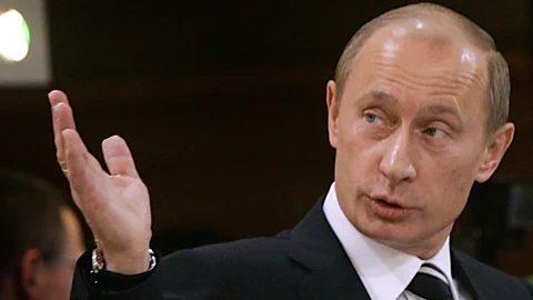 Putin spricht und hebt seine Hand.