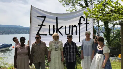 Menschen mit einem Transparent auf einer Wiese am See