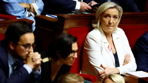 Le Pen und weitere Parlamentarier sitzen während einer Versammlung in roten Parlamentssitzen.