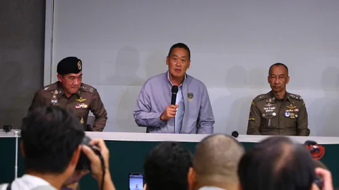 Drei Männer, darunter Premier Thavisin, halten eine Pressekonferenz, während Fotografen Bilder machen.