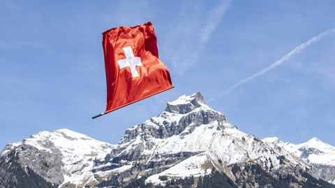 Symbolbild: Schweizer Fahne vor schneebedeckten Bergen.