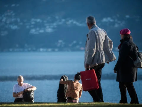 Menschen am Seeufer mit Bergen im Hintergrund.