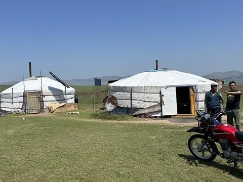 Zwei Jurten in einer weiten Landschaft mit Motorrad und zwei Personen im Vordergrund.