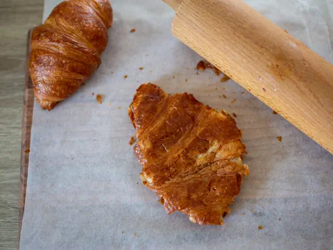 Aufgeschnittenes Croissant und Nudelholz auf Backpapier.