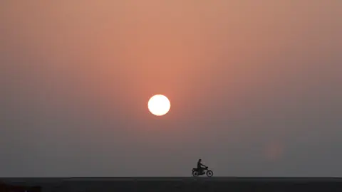 Sonne im Smog, davor auf einer Strasse ein Mopedfahrer.