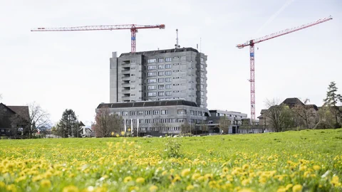 Regionalspital Wetzikon, aufnahme von draussen im Sonnenschein, davor eine Wiese voller blühendem Löwenzahn.