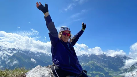 Alexandra Baumann sitzt auf einem Felsen und reckt siegesreich die Arme hoch.