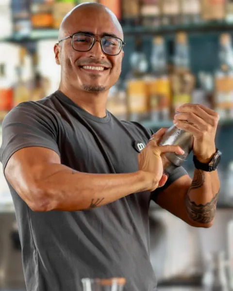 Barkeeper mit Brille und grauem T-Shirt schüttelt einen Cocktailbecher