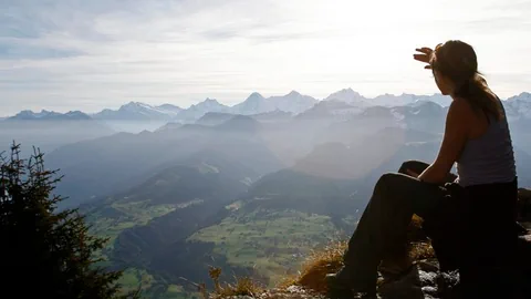 Frau sitzt auf Berggipfel und guckt in die Ferne.