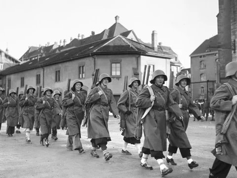 Frauen in einem Armeemantel und mit Stahlhelm marschieren in einer Kolonne. Schwarzweissbild.