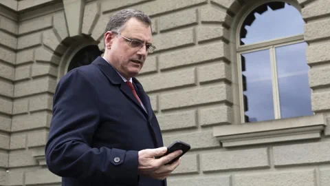 Thomas Jordan auf sein Handy schauend vor dem Bundeshaus.