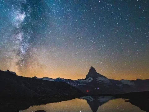 Matterhorn- ein hoher Berg – in einer Nachtaufnahme mit den Sternen. Im Vordergrund ein kleiner See.