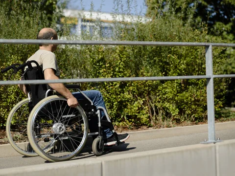 Mann im Rollstuhl neben einem Geländer im Freien.