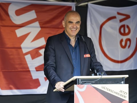 Alain Berset spricht an einem Rednerpult. Im Hintergrund sind Flaggen von Gewerkschaften zu sehen.