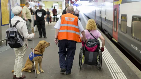 Ein Bahnhofmitarbeiter begleitet zwei Personen mit Behinderung.