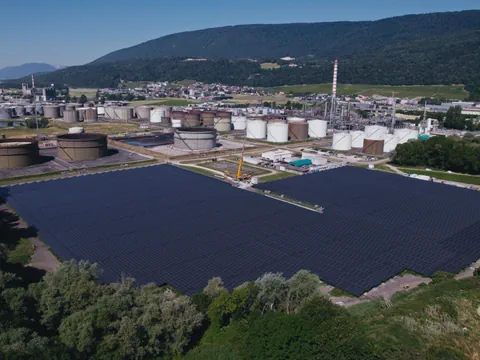 Grosse Solaranlage neben Industrietanks und Hügeln.