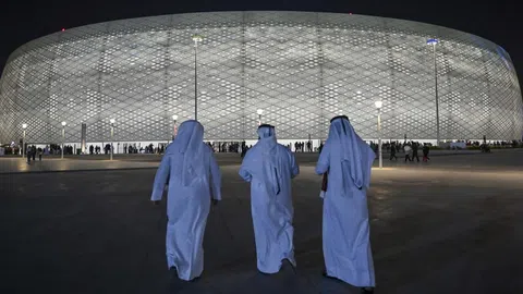 Drei Katari vor einem Fussballstadion bei Nacht.