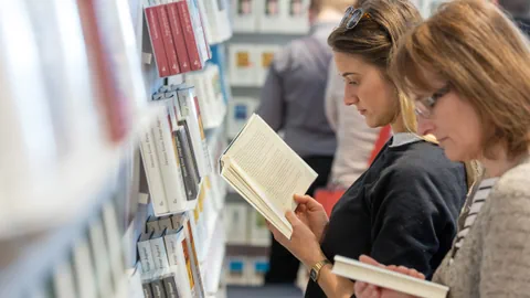 Zwei Frauen stehen lesend an einem Bücherregal