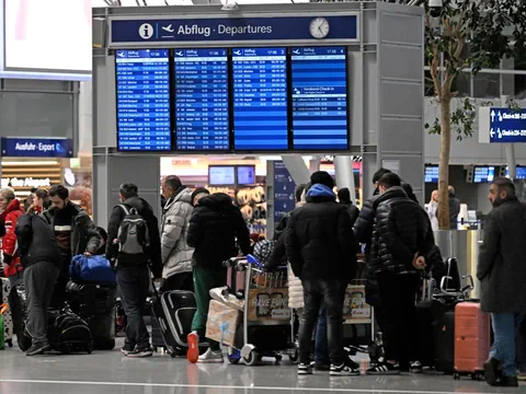 Reisende am Flughafen vor Abflugtafel mit Gepäck.