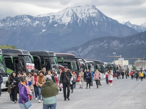 Cars sind in einer Reihe parkiert, viele Touristen stehen davor, dahinter ein Bergpanorama.