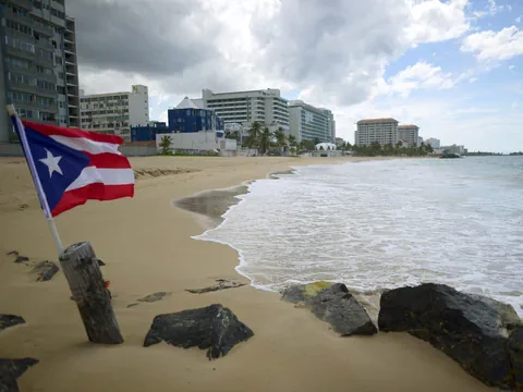 Strand mit Puerto-Rico-Flagge und Gebäuden im Hintergrund.