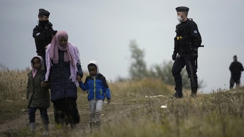 Eine Migrantin läuft mit zwei Kindern an der Hand vor zwei Polizisten.