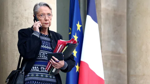 Borne am Handy vor einer EU- und einer Frankreich-Flagge.