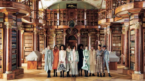 Zehn Frauen stehen in bunten Kleidern in einer historischen Bibliothek.