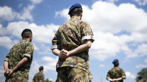 Soldaten in Tarnuniformen im Freien unter blauem Himmel.