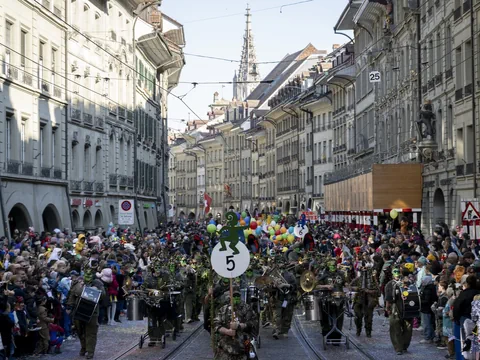 Strassenparade mit Menschenmenge und Blasmusikkapelle in einer Altstadt.